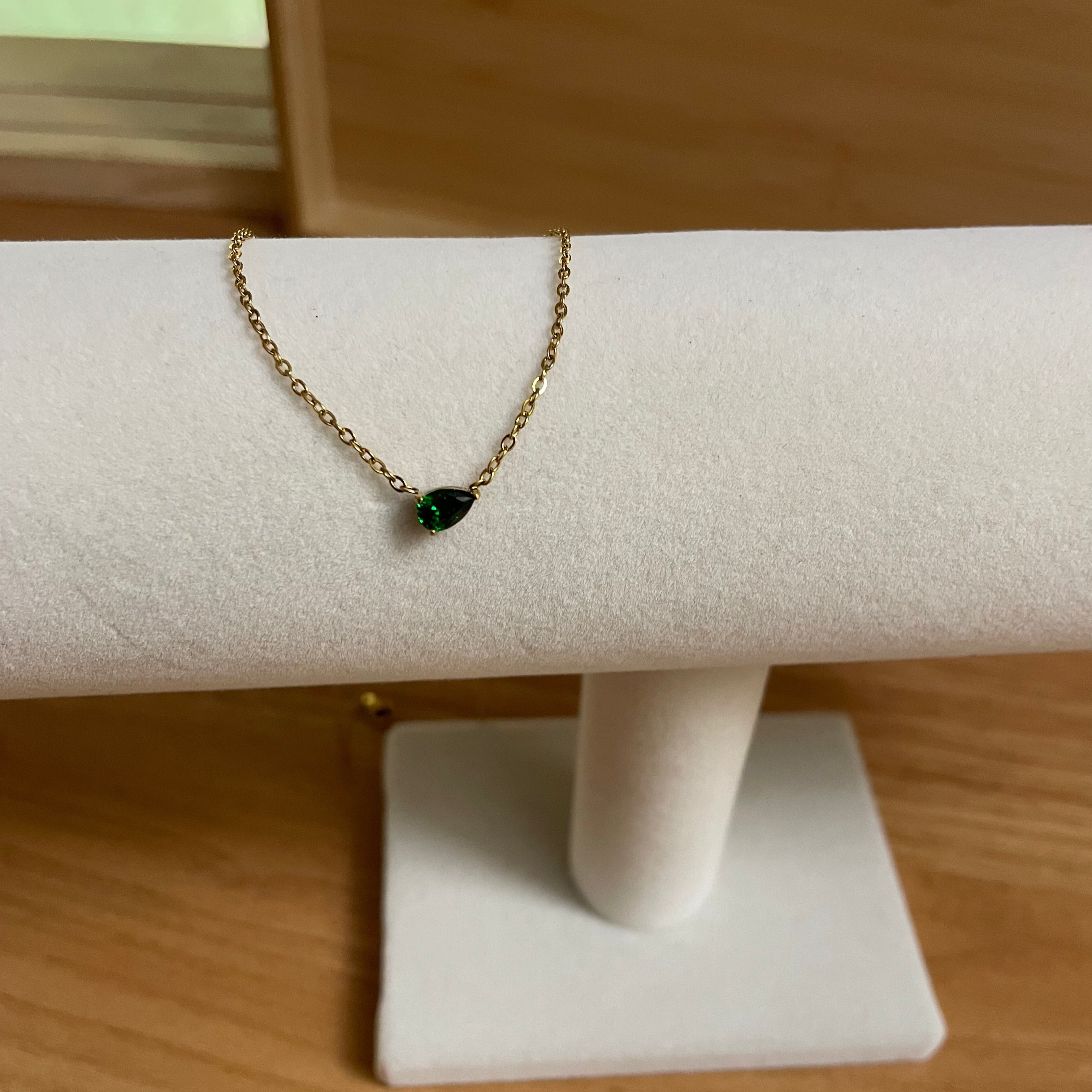 Gold bracelet with a green gemstone on a white stand against a wooden background
