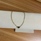Gold bracelet with a black gemstone on a white stand against a wooden background