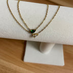 Gold necklace with a green gemstone on a white stand against a wooden background