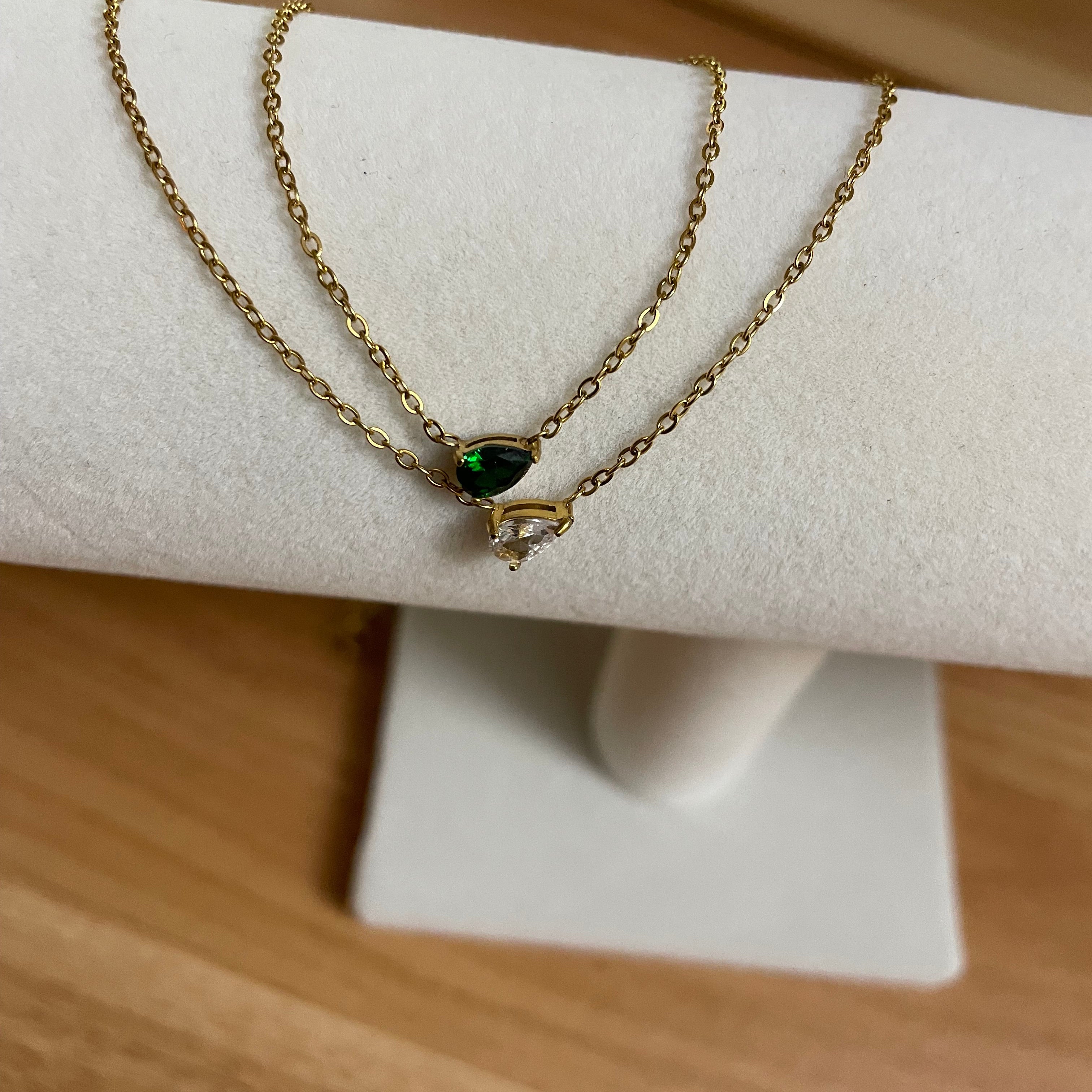 Gold necklace with a green gemstone on a white stand against a wooden background