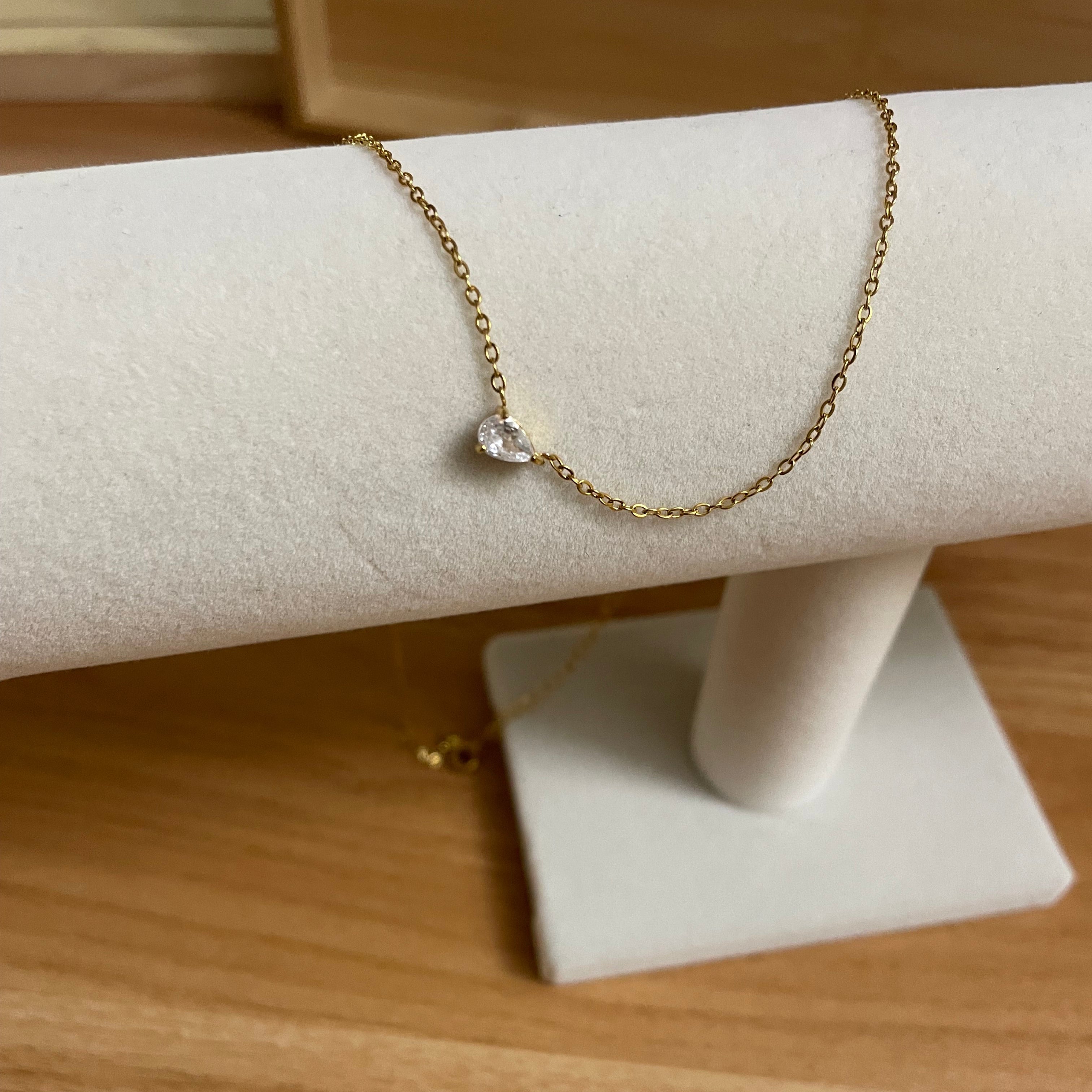 Gold bracelet with a heart-shaped pendant on a white stand against a wooden background