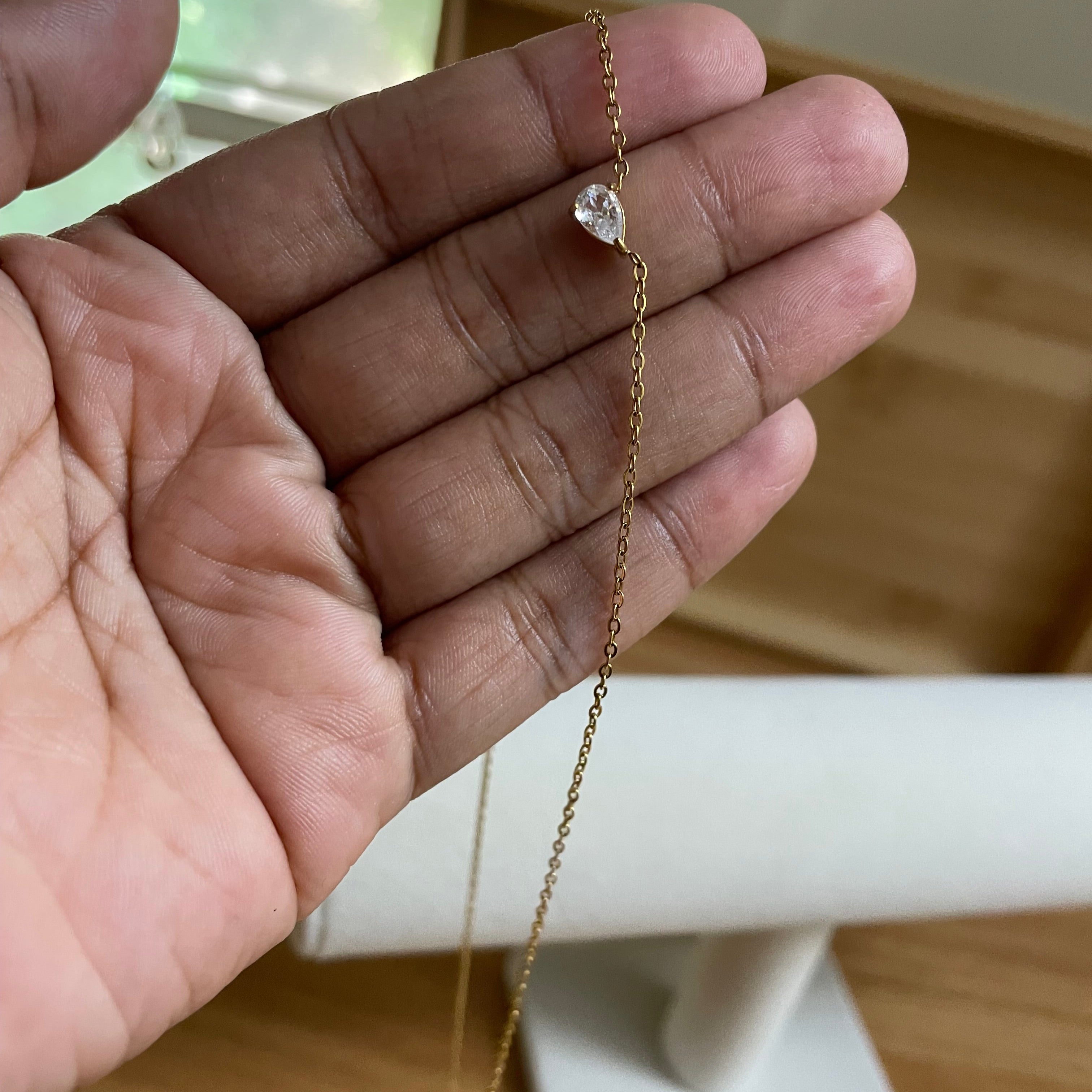 Gold necklace with a small pendant held in a hand against a neutral background